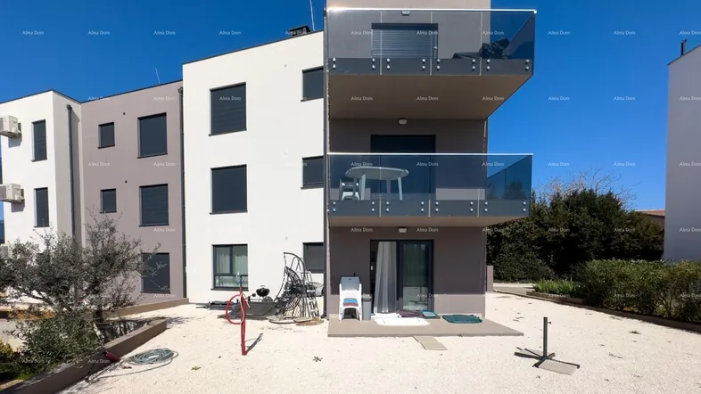 Modernes Mehrfamilienhaus mit Balkonen und einer Kiesfläche im Außenbereich unter blauem Himmel.