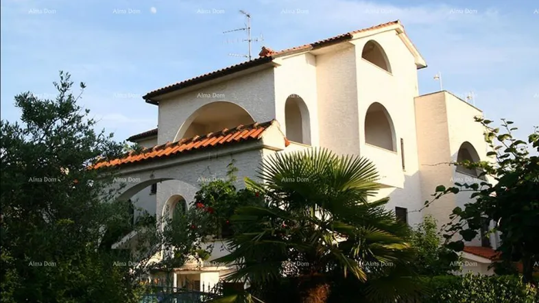 Weißes Haus mit roten Ziegeldächern und markanten Bögen, umgeben von üppiger mediterraner Vegetation.