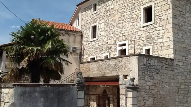 Traditionelle Steinhausfassade mit mehreren Fenstern und einem Eingangsbereich, umgeben von einer Steinmauer.