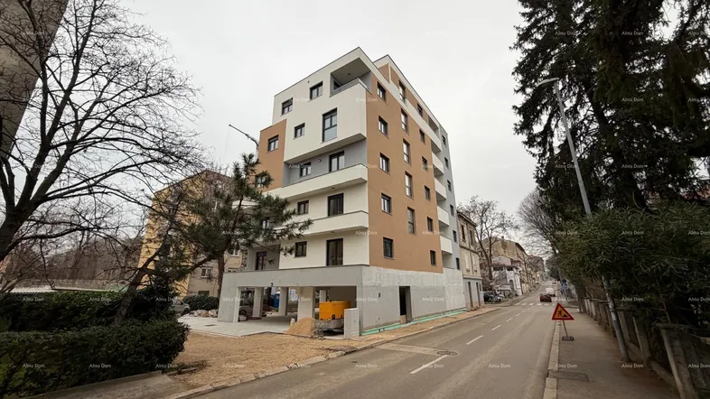 Modernes Mehrfamilienhaus im Bauzustand mit mehreren Etagen und Balkonen an einer Straße.