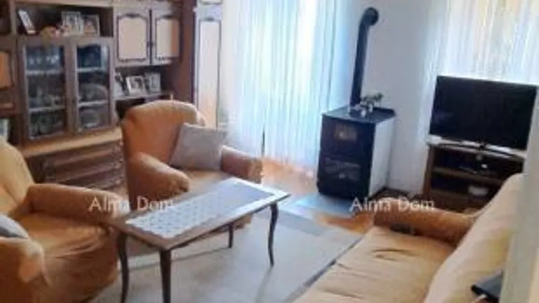 Gemütliches Wohnzimmer mit beigen Sofas, Holzboden und einem traditionellen Kaminofen.