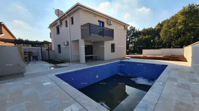 Modernes Einfamilienhaus mit privatem Pool und großzügiger Terrasse, umgeben von Grünflächen.
