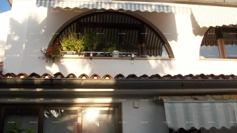 Fassade eines Hauses mit bogenförmigen Fenstern, Blumenkästen und gestreiften Markisen.