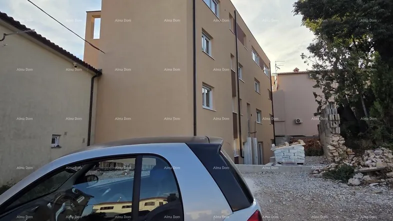 Neubaugebäude mit beiger Fassade und sichtbaren Bauarbeiten, ein Auto im Vordergrund.
