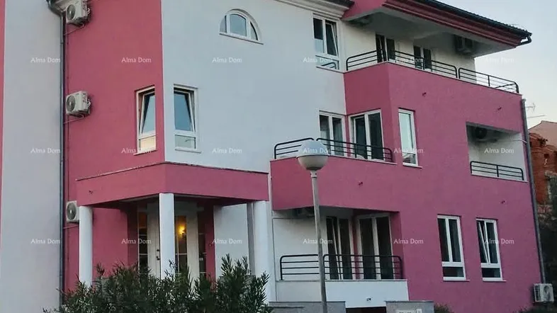 Modernes Gebäude mit rosa und weißen Fassaden, mehreren Balkonen und sichtbaren Klimaanlagen.