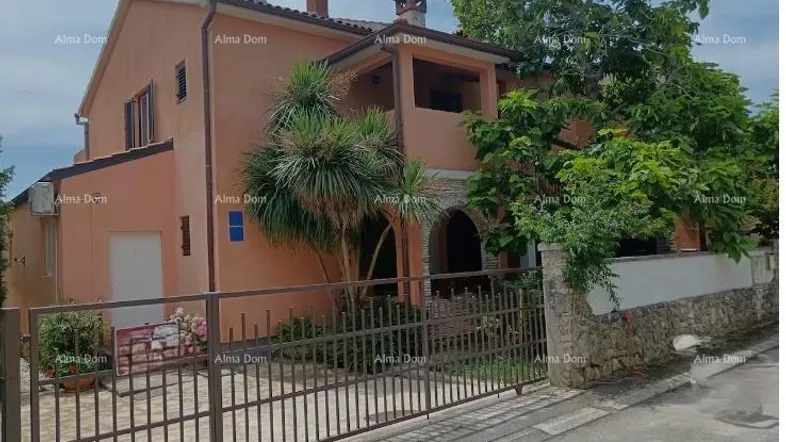 Ein charmantes Haus mit orangefarbener Fassade, umgeben von mediterraner Vegetation und einem Metallzaun.