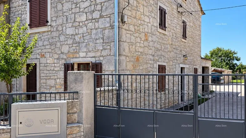 Traditionelles Steinhaus mit braunen Fensterläden und einem modernen Metalltor unter blauem Himmel.