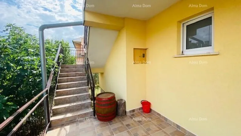 Außenbereich mit gefliester Terrasse und Treppe zum oberen Stockwerk unter blauem Himmel.