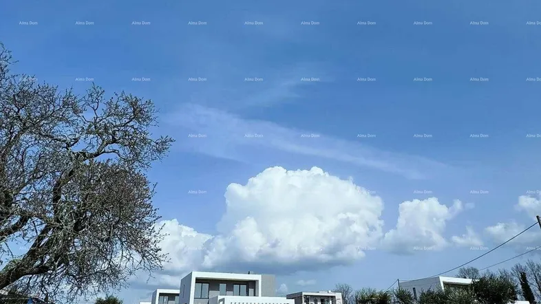 Moderne Häuser unter blauem Himmel mit großen Wolken und einer Steinmauer im Vordergrund.