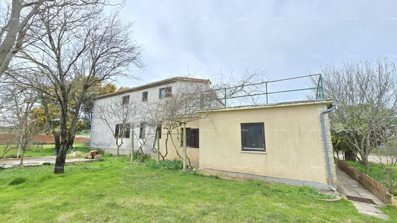 Ländliches Haus mit einfacher Fassade und großem Grundstück unter bewölktem Himmel.