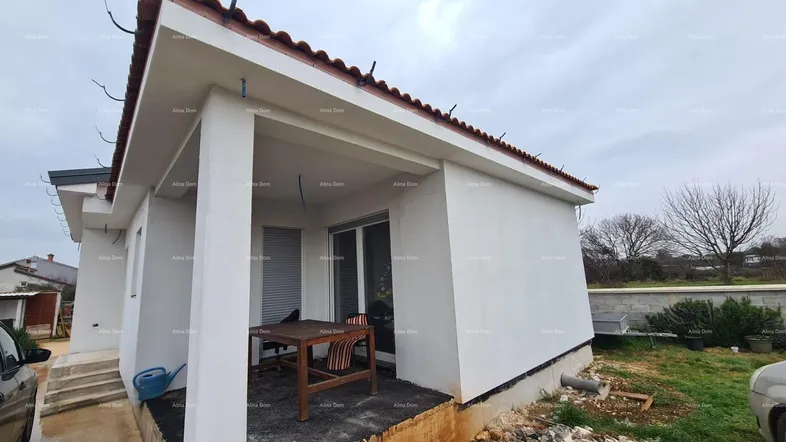 Überdachte Terrasse eines im Bau befindlichen Hauses mit provisorischen Möbeln und Blick auf den Garten.