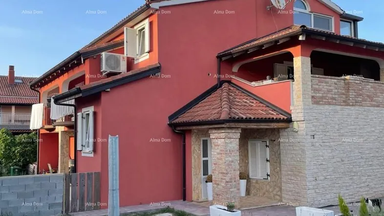 Rote Fassade des Hauses mit Steinelementen und einem kleinen Gartenbereich unter blauem Himmel.