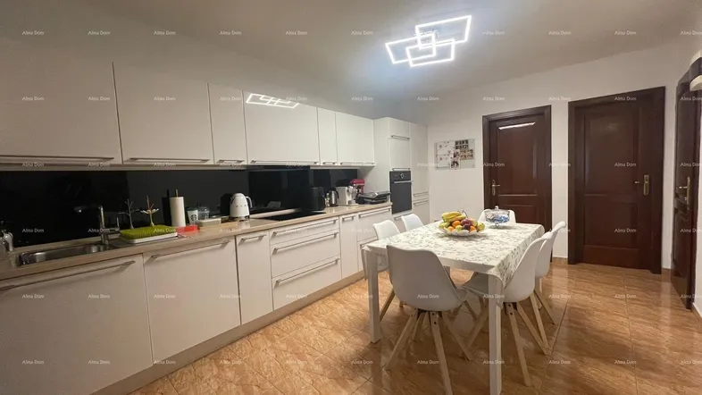 Moderne Einbauküche mit weißen Schränken, dunkler Arbeitsplatte und Essbereich mit Fliesenboden.