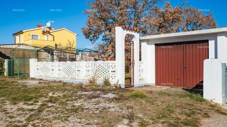Außenansicht des Grundstücks mit weißem Zaun, braunem Garagentor und einem gelben Haus im Hintergrund.