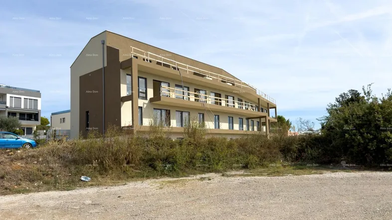 Modernes Mehrfamilienhaus mit mehreren Balkonen und heller Fassade, umgeben von unbebautem Land.