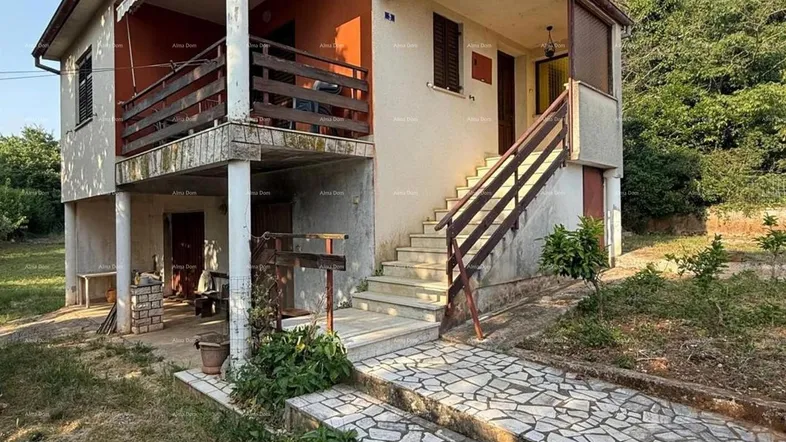 Zweistöckiges Haus mit Balkon, Außentreppe und Gartenbereich in ländlicher Umgebung.