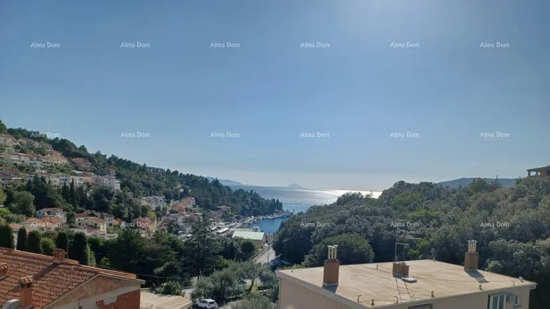 Weitläufiger Blick über die Küstenstadt, das Meer und die umliegenden grünen Hügel unter blauem Himmel.