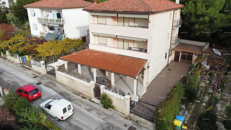 Luftaufnahme eines Wohnhauses mit rotem Ziegeldach und umliegender Straße in grüner Umgebung.