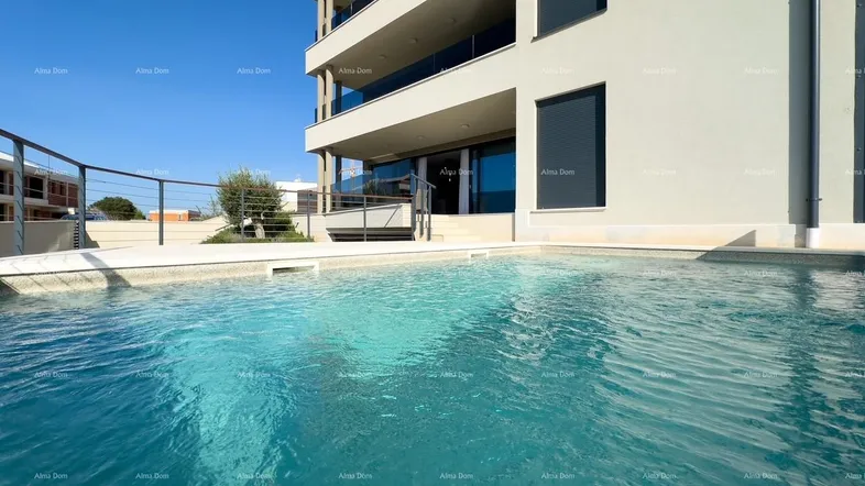 Moderner Apartmentkomplex mit Außenpool und klarem blauen Wasser unter strahlendem Himmel.