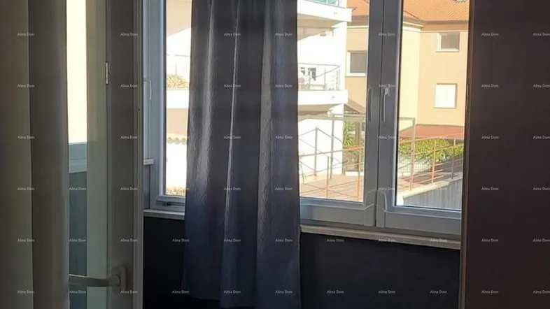 Blick durch eine Glasschiebetür auf einen gefliesten Balkon mit Vorhängen und Tageslicht.