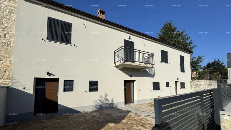 Moderne Hausfassade mit hellen Wänden, dunklen Fensterläden und einem kleinen Balkon.