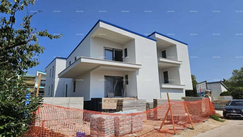 Modernes Gebäude im Bau mit weißer Fassade und blauen Akzenten unter klarem Himmel.