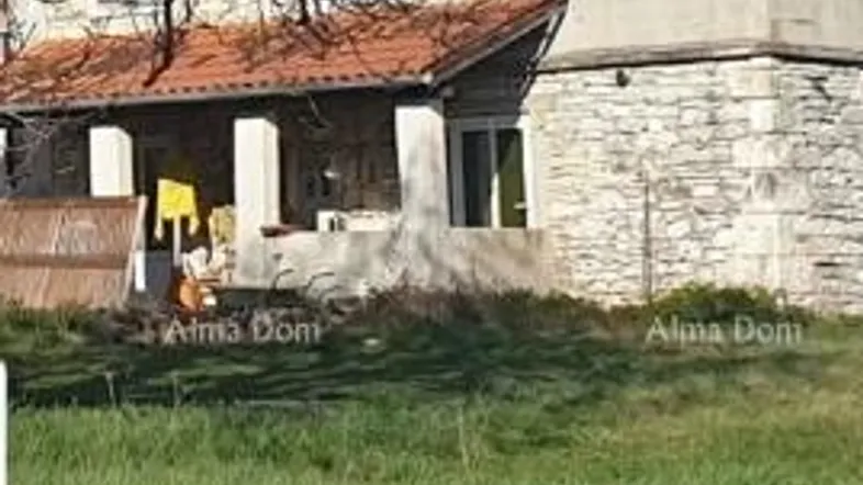 Traditionelles Steinhaus mit rustikaler Architektur und überdachtem Eingangsbereich, umgeben von Grünflächen.