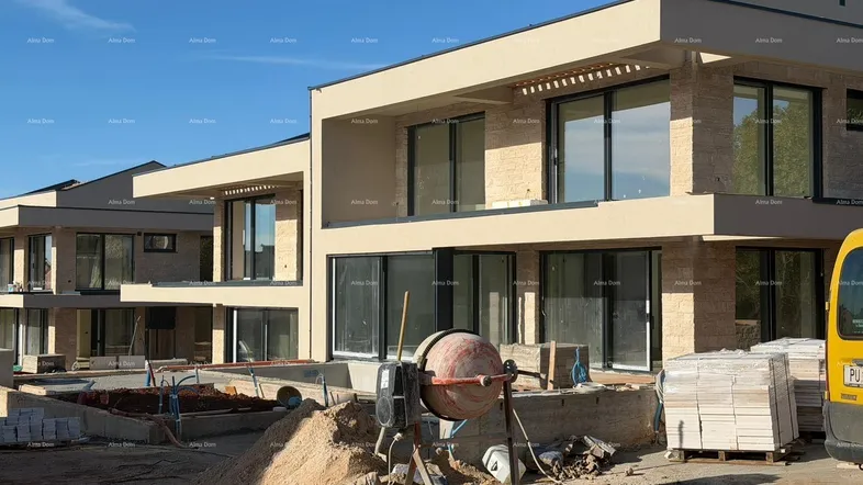 Moderne Villen im Bau mit großen Fenstern und beiger Fassade unter blauem Himmel.
