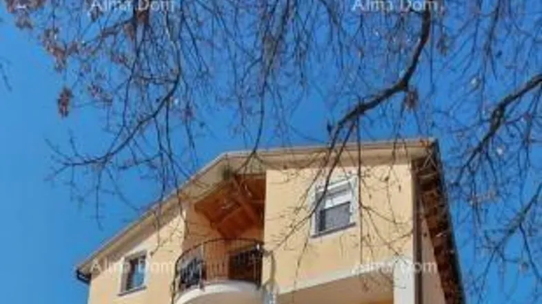 Gelbes Mehrfamilienhaus mit mehreren Balkonen unter blauem Himmel und kahlen Bäumen.