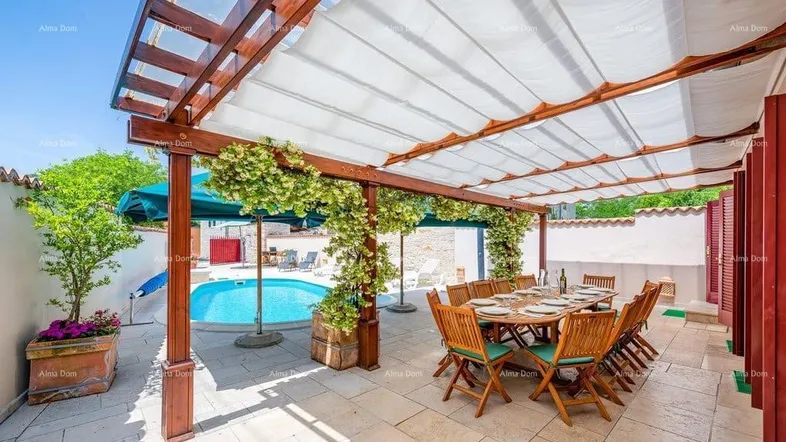 Überdachte Terrasse mit großem Esstisch und Blick auf den Poolbereich.