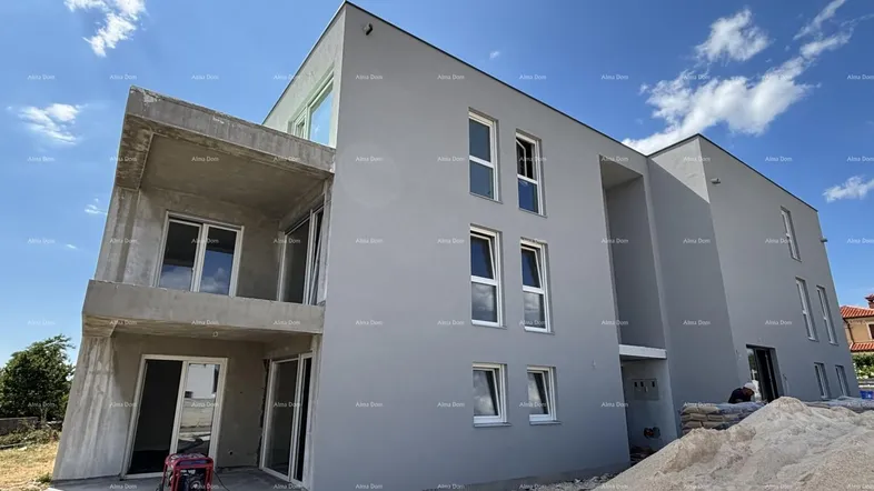 Moderne Fassade eines im Bau befindlichen Gebäudes mit grauer Putzfassade und weißen Fenstern unter blauem Himmel.