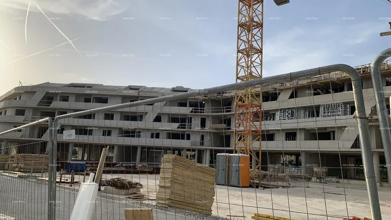 Baustelle eines modernen Gebäudekomplexes mit Kran und Baumaterialien unter strahlendem Himmel.