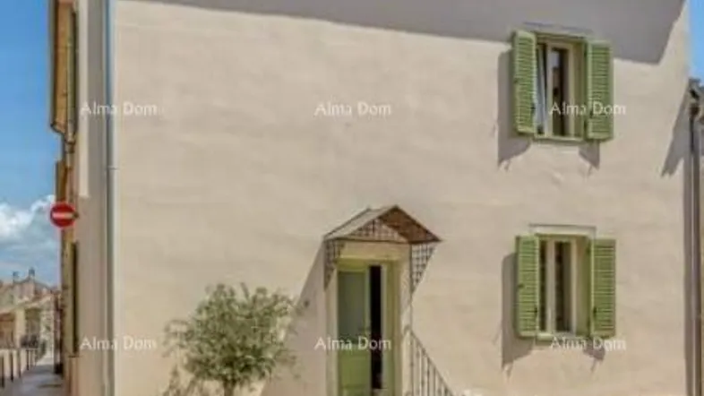 Traditionelles Haus mit beiger Fassade, grünen Fensterläden und Dachgauben in einer charmanten Gasse.