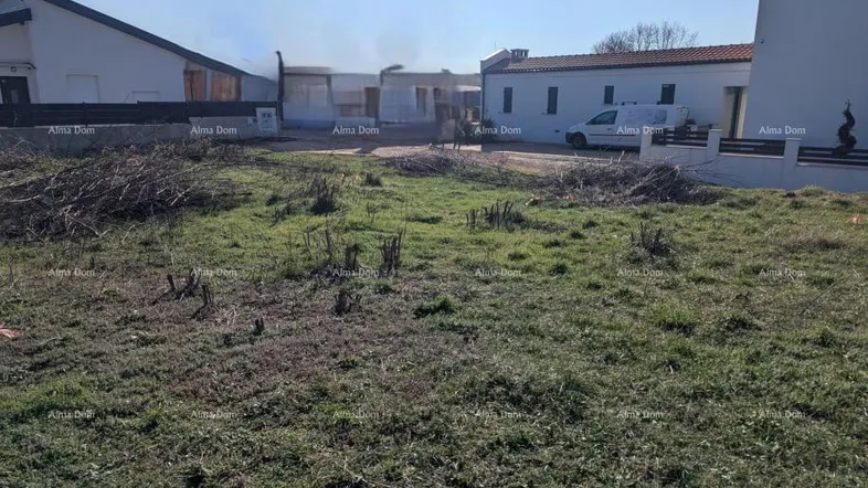 Blick auf ein unbebautes Grundstück mit Gras und Gestrüpp, umgeben von Wohnhäusern unter blauem Himmel.
