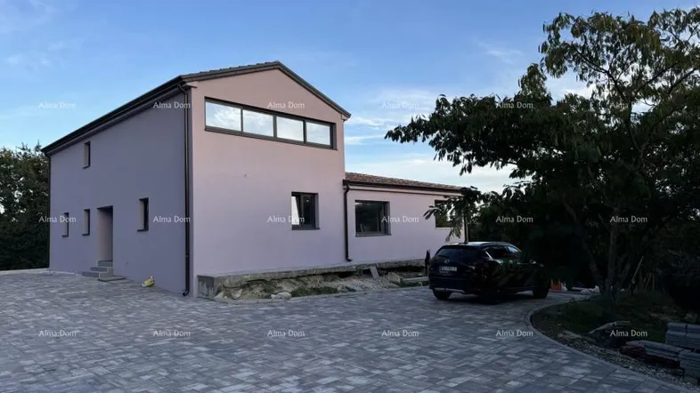 Modernes Haus mit gepflasterter Auffahrt und umliegender Natur unter blauem Himmel.