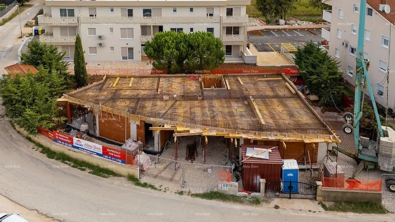 Luftaufnahme einer Baustelle mit Rohbau und Bewehrungsstahl für die nächste Betondecke, umgeben von Gebäuden.