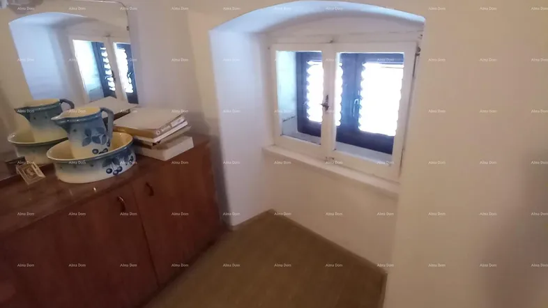 Kleines Schlafzimmer mit Holzboden, Kommode und einem Fenster mit Rundbogen.