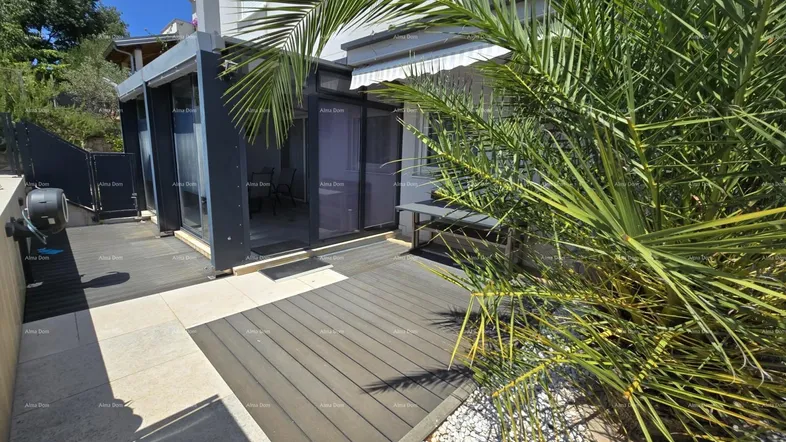 Geräumige Terrasse mit Holzoptik-Bodenbelag, umgeben von mediterraner Bepflanzung und einem Palmenbaum.