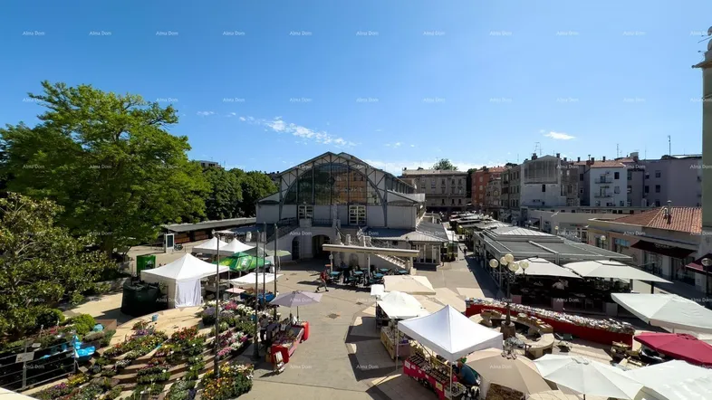 Weitläufiger Blick auf einen belebten Marktplatz mit verschiedenen Ständen und umliegenden Gebäuden unter blauem Himmel.
