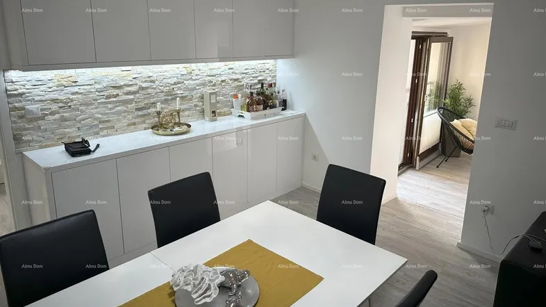 Moderner Essbereich mit weißem Tisch, schwarzen Stühlen und einer Steinwand als Akzentbeleuchtung.