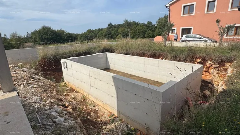 Baustelle mit ausgehobenem Poolfundament und bestehendem Haus im Hintergrund unter blauem Himmel.