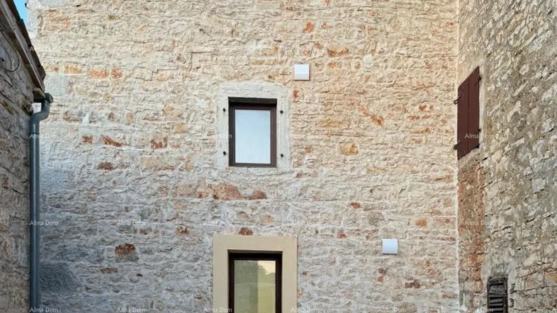 Historische Steinfassade eines Gebäudes mit einem modernen Eingang und einem kleinen gepflasterten Vorplatz.