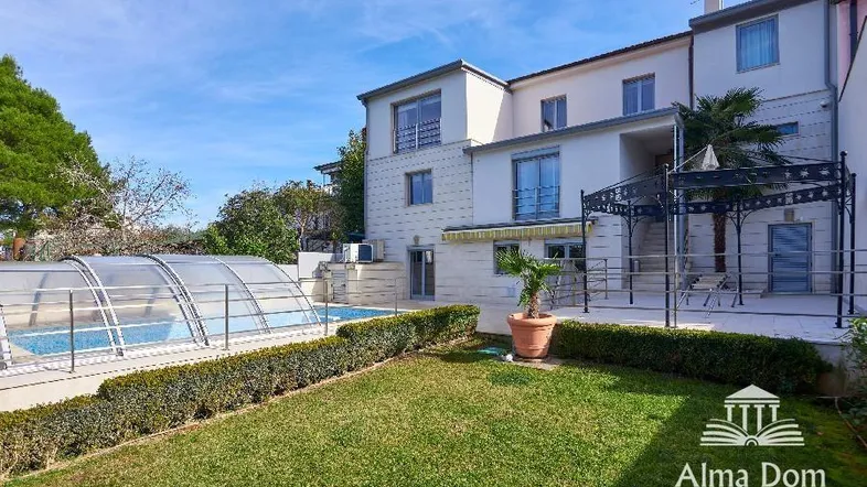 Gepflegter Gartenbereich mit Rasenfläche, Hecken und einem überdachten Swimmingpool neben dem Haus.