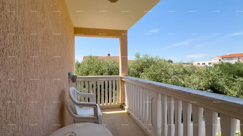 Balkon mit Tisch und Stühlen, umgeben von grünen Bäumen unter blauem Himmel.