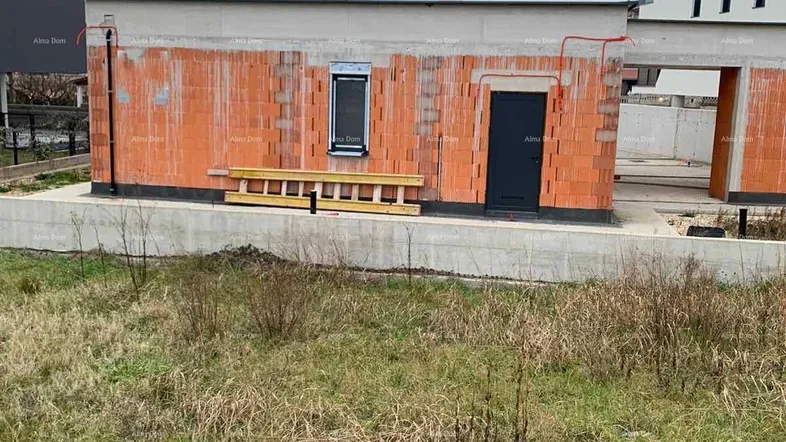 Ein im Bau befindliches Gebäude mit Ziegelwänden und einem Fenster, umgeben von Gras.