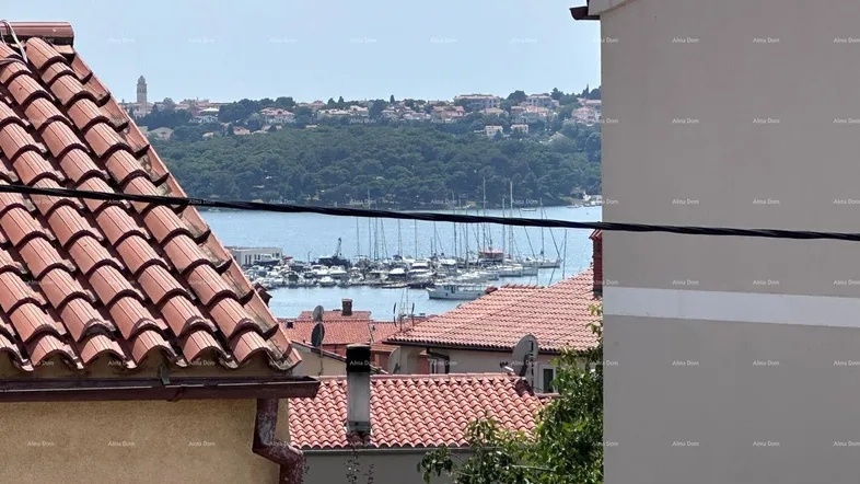 Blick über rote Dächer auf das weite Meer und einen belebten Hafen mit vielen Booten.