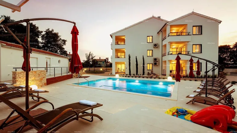Abendliche Ansicht des Apartmentgebäudes mit beleuchtetem Poolbereich und Liegestühlen.