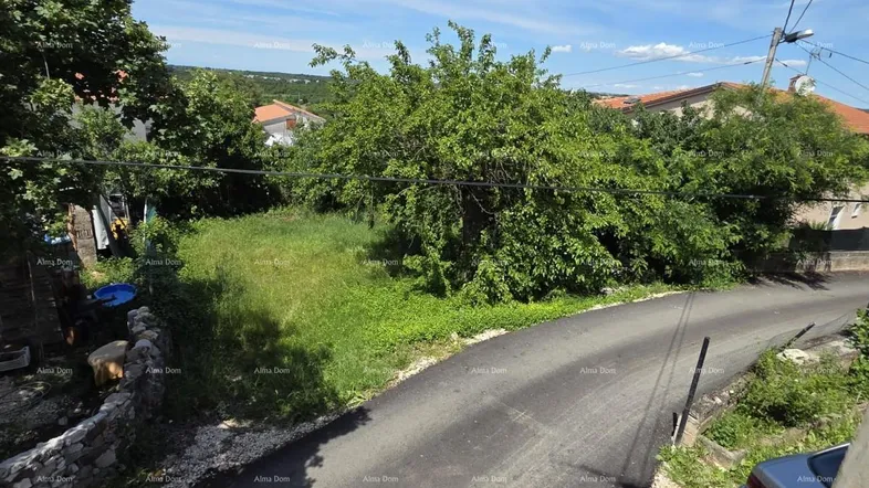 Blick auf eine kurvige Landstraße, umgeben von üppigem Grün und Häusern in der Ferne unter blauem Himmel.