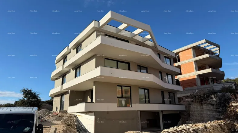 Modernes Mehrfamilienhaus im Bau mit geschwungenen Balkonen und Baustellenumgebung unter blauem Himmel.