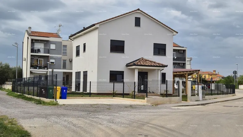 Modernes Wohnhaus mit weißer Fassade und dunklen Fensterläden unter bewölktem Himmel.